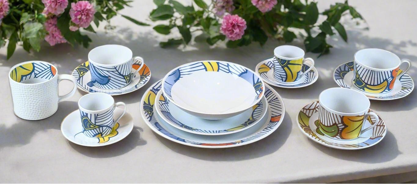 Vaisselle et assiettes avec le motif wax fleur de mariage, sur une table blanche dans un jardin ensoleillé avec des fleurs dans le fond.