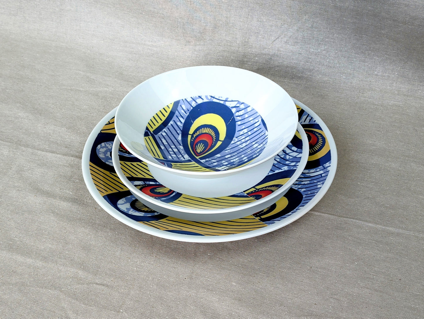 Coffret d'assiettes rondes en porcelaine fine Française fabriquées à la demande avec motif anneaux larges WAX d'afrique "Nos destins entrelacés" dans coffret de 6 assiettes.