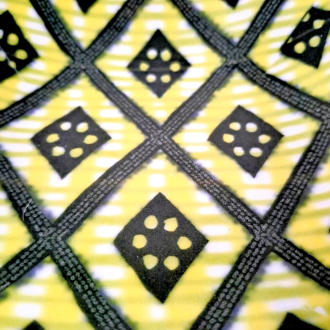Gros plan du motif Ìbùkúnolúwa, treillis noir et vert olive sur fond jaune citron, losanges percés de points