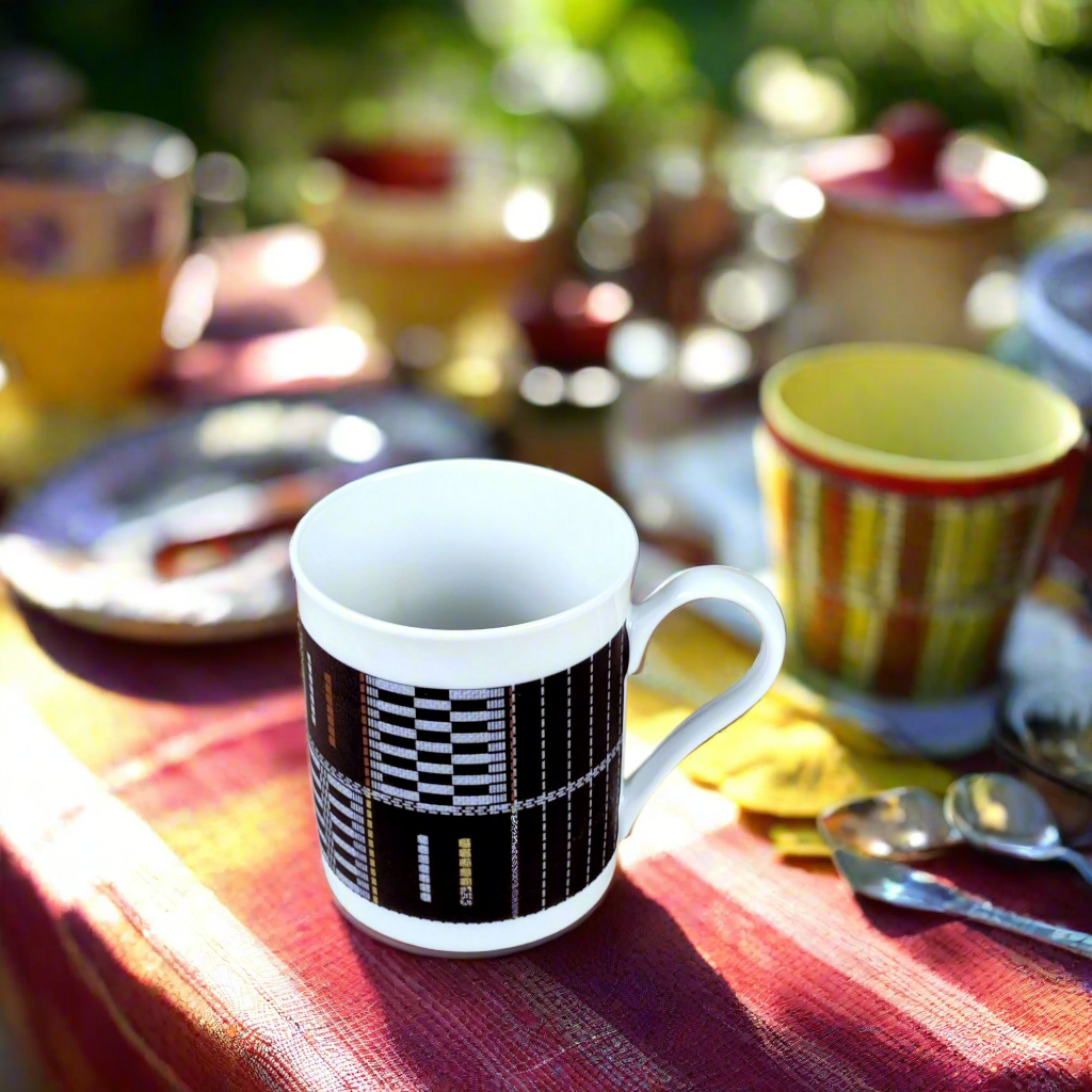 Vue de trois quarts : mug Sénoufo noir et blanc sur nappe rouge, bols rayés et couverts sur table de fête