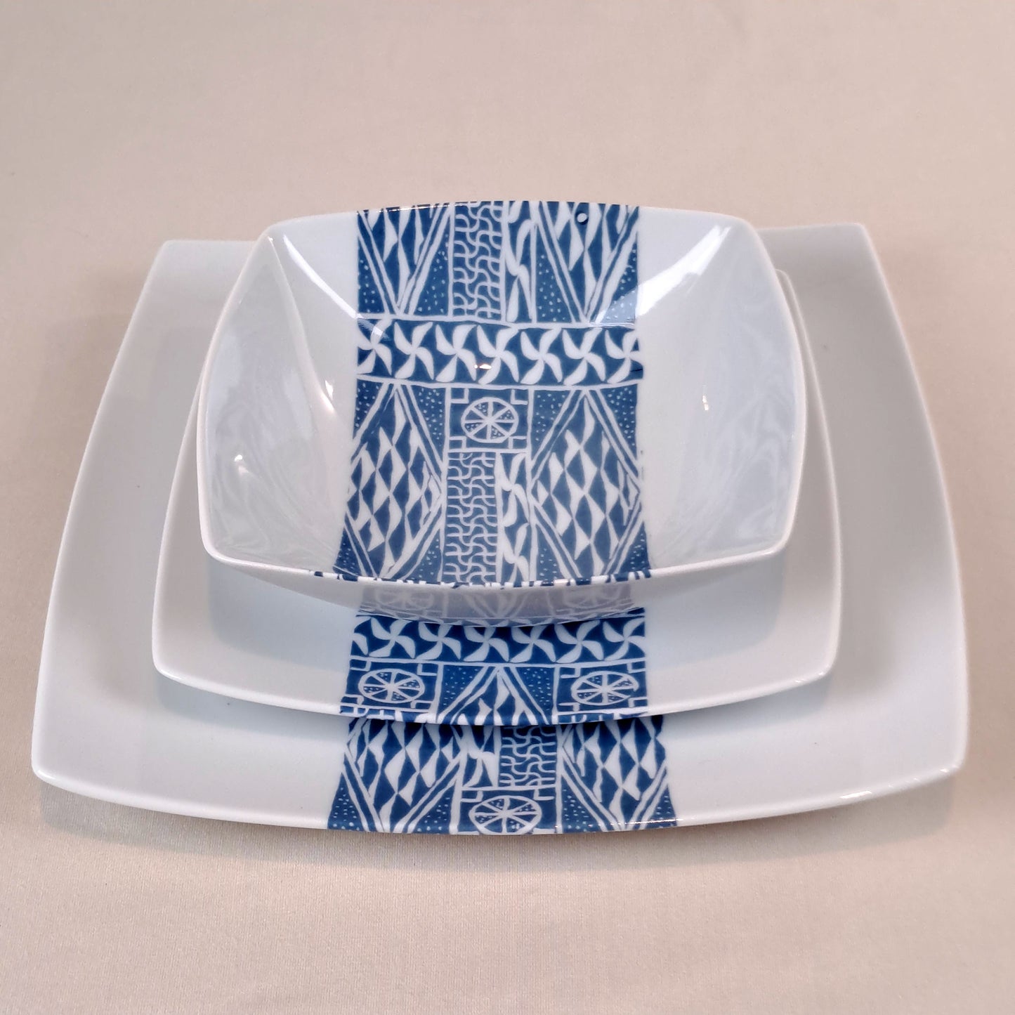 Coffret d'assiettes carrées en porcelaine fine Française fabriquées à la demande avec motif bande ethnique d'Afrique "Ndop" bleu du Cameroun, présenté dans un coffret de 6 assiettes.