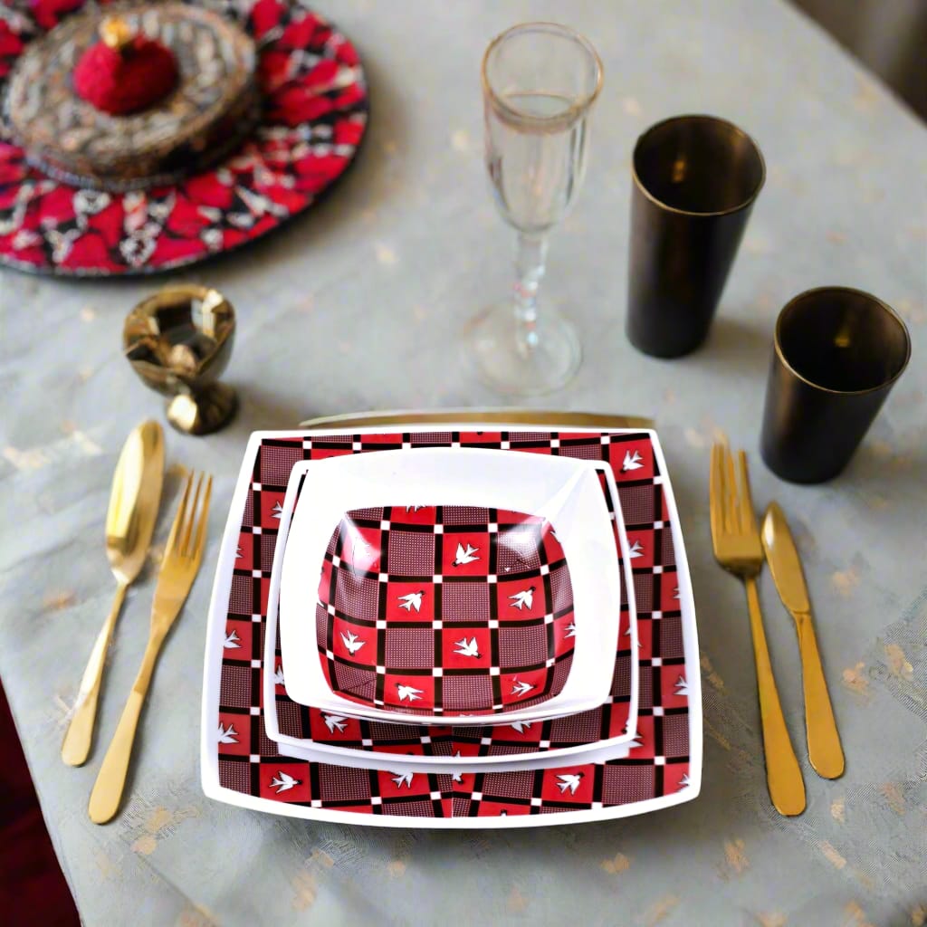 Vue zénithale : bol et assiettes carrées Luili rouge et brun sur nappe grise, couverts laiton et gobelets noirs