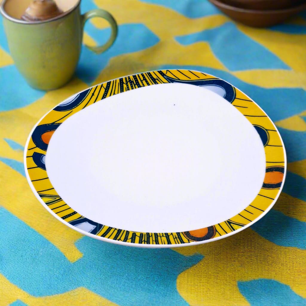 Vue de face légèrement plongeante de l'assiette ovale Electric Bulb jaune sur nappe turquoise et jaune, mug vert