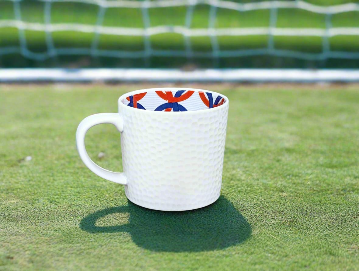 Vue rasante : mug grenaillé Anneaux entrelacés sur gazon au soleil, filet de but flou en arrière-plan